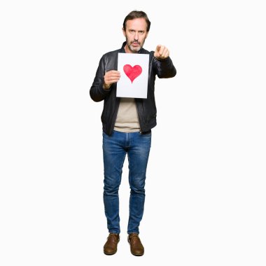 Yakışıklı orta yaş erkek holding kağıt kırmızı kalp kamera ve size parmak ile işaret ile el işareti, pozitif ve kendinden emin bir jest ön