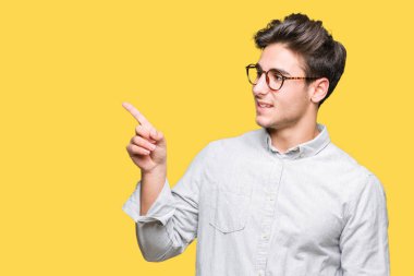 Kameraya bakarak yan el ve parmak ile işaret yüzünde kocaman bir gülümseme ile izole arka plan üzerinde gözlük takan genç yakışıklı adam.