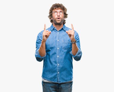 İzole arka plan üzerinde gözlük takan yakışıklı İspanyol modeli adam hayret ve yukarıya bakıp parmakları ile işaret şaşırttı ve silah kaldırdı.