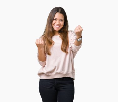 Üzerinde pembe kazak giyen genç güzel esmer kadın gülümseyerek ve başarı için çığlık arka plan çok mutlu ve heyecanlı kaldırdı, silah ile kazanan jest yapıyor izole. Kutlama kavramı.