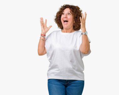 Üzerinde beyaz t-shirt giyen güzel orta ager üst düzey kadın deli kutluyor arka plan izole ve başarı için kaldırdı kollarını açarak hayrete ve heyecanlı çığlık gözleri açık. Kazanan kavramı