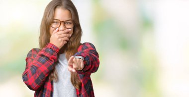 Ceket ve gözlük izole üzerinde giyen genç güzel esmer kadın arka plan sizin parmak el kamerasıyla ağzına, utanç ifadesi işaret eden gülme