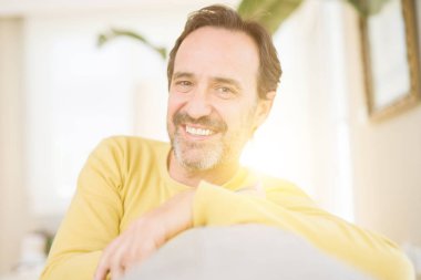 Rahat ve evde kameraya gülümseyen kanepede oturan yakışıklı orta yaş adam