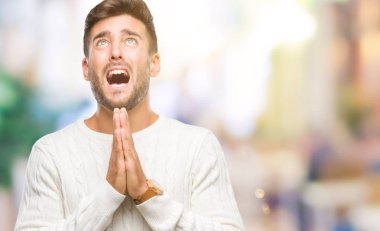 Genç yakışıklı adam yalvarıyor ve umut ifade yüzünde çok duygusal ve endişe ile birlikte elleriyle dua izole arka plan üzerinde kış kazak giyiyor. Bağışlanmak. Din kavramı.