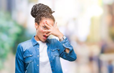 Genç mahcup ifadeyle parmaklarımın arasından seyir gözlüklü yüz ve gözler el ile kapsayan şok bakmak izole arka plan üzerinde saç Afro-Amerikan Kız örgülü.