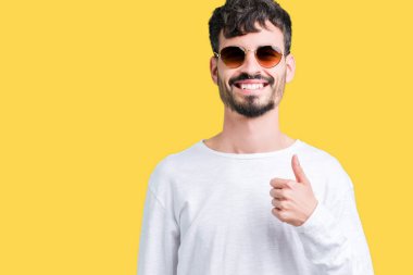 Genç yakışıklı adam hareketi el ile mutlu yaşasın yapıyor izole arka plan üzerinde güneş gözlüğü takıyor. Kameraya bakarak başarı gösteren ile ifade onaylama.