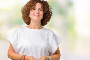 Arka plan eller üzerinde beyaz t-shirt giyen güzel orta ager üst düzey kadın birlikte izole ve rahat ve neşeli gülümseyen parmak çarpı işareti. Başarı ve iyimser