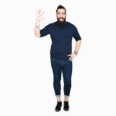 Uzun saç ve sakal gülümseyen bardakları ve boyutu işaret parmaklı ararken ve kamera işi el ile kendine güvenen el hareketi giyen genç hipster adam. Ölçü kavramı.