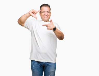 Orta yaş Arap adam wearig t-shirt elle yapma çerçeve ve parmakları ile mutlu yüz gülümseyen izole arka plan üzerinde beyaz. Yaratıcılık ve Fotoğrafçılık kavramı.