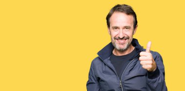 Orta yaş yakışıklı adam mutlu yaşasın el ile jest yapmak bir ceket giyiyor. Başarı gösteren kameraya bakarak ifade onaylama.