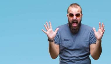 Üzerinde güneş gözlüğü takmış Genç beyaz hipster adam deli kutluyor arka plan izole ve çığlık kaldırdı ve açık gözleri heyecanlı silah ile başarı için hayrete düşürdü. Kazanan kavramı