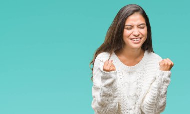 Üzerinde kış kazak giyen genç güzel Arap kadın gülümseyerek ve başarı için çığlık arka plan çok mutlu ve heyecanlı kaldırdı, silah ile kazanan jest yapıyor izole. Kutlama kavramı.