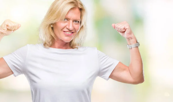 Middle age blonde woman over isolated background showing arms muscles smiling proud. Fitness concept.