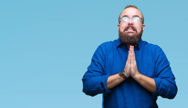 Young caucasian hipster man wearing glasses over isolated background begging and praying with hands together with hope expression on face very emotional and worried. Asking for forgiveness. Religion concept.