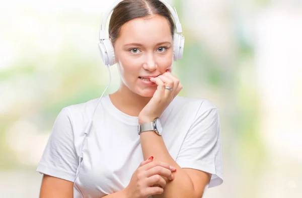 年轻的白种人妇女听音乐戴着耳机在孤立的背景下看紧张和紧张与手在嘴咬指甲 焦虑问题 — 图库照片