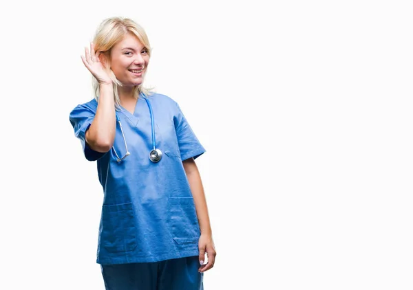 年轻美丽的金发碧眼的医生妇女穿着医疗制服在孤立的背景微笑着用手耳朵听谣言或流言蜚语 耳聋概念 — 图库照片
