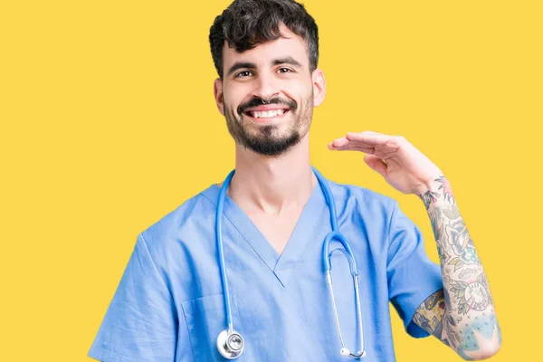 Young handsome nurse man wearing surgeon uniform over isolated background gesturing with hands showing big and large size sign, measure symbol. Smiling looking at the camera. Measuring concept.