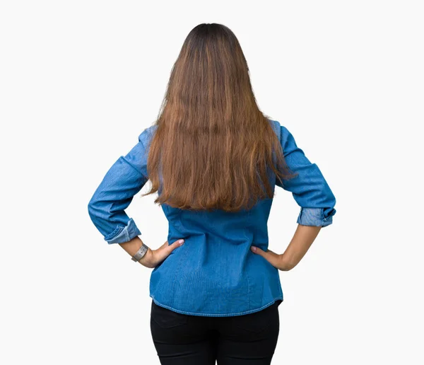 年轻美丽的黑发女人穿着蓝色粗斜纹棉布衬衫在孤立的背景站向后看远离与手臂在身体 — 图库照片