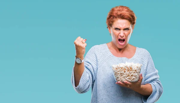 活跃的高级高加索红发妇女吃爆米花在孤立的背景恼火和沮丧的喊声与愤怒 疯狂和大喊大叫与提高的手 愤怒的概念 — 图库照片
