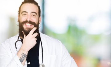 Doktor tıbbi ceket ve emin çapraz kollar ve çeneme kaldırdı el ile gülümseme ile kamera seyir stetoskop uzun saçlı. Pozitif düşünce.