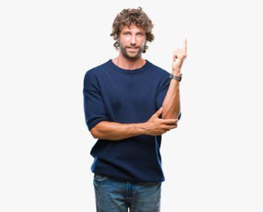 Yüzünde kocaman bir gülümseme ile izole arka plan üzerinde kış kazak giyen yakışıklı İspanyol modeli adam kameraya bakarak yan el ve parmak ile işaret.