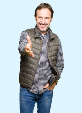 Orta yaş yakışıklı adam olarak tebrik ve konuksever dost sunan karşılıklı gülümseyen kış yelek giyiyor. Başarılı iş.