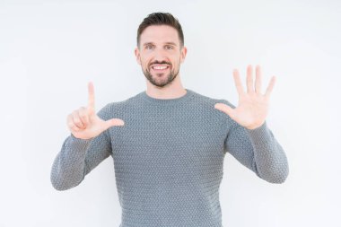Gösterilen ve parmakları ile işaret izole arka plan üzerinde rahat kazak giyen genç yakışıklı adam kendinden emin ve mutlu gülümseyerek süre yedi numara.