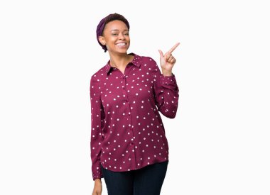 Kameraya bakarak yan el ve parmak ile işaret eden başörtüsü yüzünde kocaman bir gülümseme ile izole arka plan üzerinde giyen güzel genç Afro-Amerikan kadın.