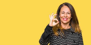 Güzel orta yaş giyen moda ceket el ve parmaklar ok işaretiyle yapıyor olumlu gülümseyen kadın. Başarılı ifade.