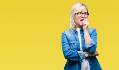 Stresli ve gergin elle çivi ısırma ağzına bakarak izole arka plan üzerinde gözlük takan genç güzel sarışın bir kadın. Anksiyete sorunu.