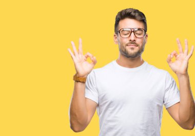 Genç yakışıklı adam gözlük izole arka plan üzerinde dinlenmek ve gülümseyen gözlerle parmak ile meditasyon jest yapıyor kapalı. Yoga kavramı.