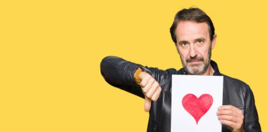 Başparmak aşağı, ret kavramı ile eksi işareti gösterilen yakışıklı orta yaş erkek holding kağıt kızgın yüzü ile kırmızı kalpli sevmemek