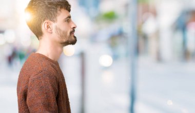 Genç yakışıklı adam giyen kış kazak izole arka tarafına, seyir üzerinde dinlenmek doğal yüz emin gülümseme ile pozuyla profili.