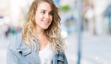 Üzerinde kot ceket giyen güzel genç sarışın kadın arka plan uzak tarafına gülümseme ile yüzünde, doğal ifade arıyorum izole. Kendine güvenen gülüyor.