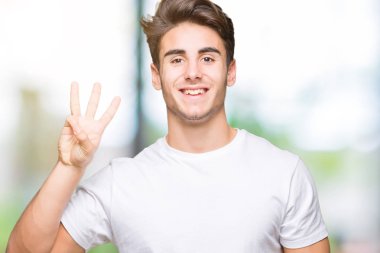 Gösterilen ve parmakları ile işaret izole arka plan üzerinde beyaz t-shirt giyen genç yakışıklı adam kendinden emin ve mutlu gülümseyerek iken üçüncü.