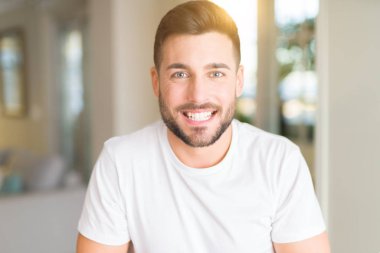 Casual beyaz t-shirt evde mutlu ve güzel bir gülümseme ile yüzünde giyen genç yakışıklı adam. Şanslı kişi.