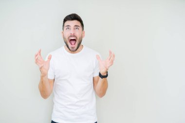 Üzerinde rahat beyaz t-shirt giyen genç yakışıklı adam arka plan deli izole ve deli bağırarak ve agresif ifade ve silah kaldırdı bağırıyor. Hayal kırıklığı kavramı.