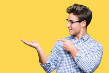 Hayret ve el ile sunulması ve parmak ile işaret ederken kameraya gülümseyen izole arka plan üzerinde gözlük takan genç yakışıklı adam.