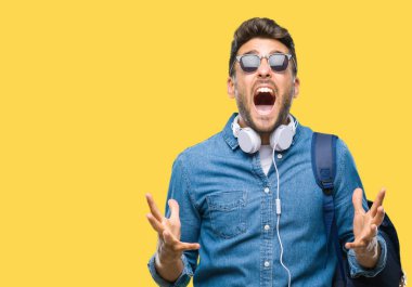 Üzerinde kulaklık ve sırt çantası giyen genç yakışıklı turist adam arka plan deli izole ve deli bağırarak ve agresif ifade ve silah kaldırdı bağırıyor. Hayal kırıklığı kavramı.