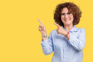 Gülümseyen ve iki elleri ve parmakları ile tarafına işaret kamera bakarak izole arka plan üzerinde gözlük güzel orta ager üst düzey businees kadın.