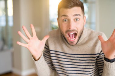 Yakışıklı genç adam evde çok mutlu ve heyecanlı, kocaman bir gülümseme ile çığlık ve ellerini kaldırdı zaferini kutluyor kazanan ifade