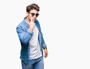 Genç yakışıklı adam giyen güneş gözlüğü izole üzerinde arka plan işaret jest göz izlemek için şüpheli ifade