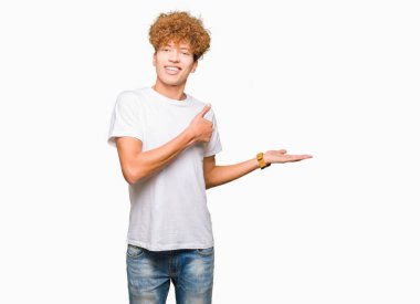 Casual beyaz t-shirt gösteren giyen afro saçlı yakışıklı delikanlı palm el ve yukarıya, mutlu ve neşeli gülümseyen baş parmakları Tamam jest yapıyor