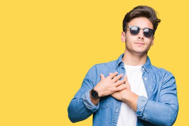 Yakışıklı delikanlı ile gülümseyen izole arka plan üzerinde güneş gözlüğü takıyor kapalı gözler ve yüzünde minnettar jest ile göğüs üzerinde eller. Sağlık kavramı.