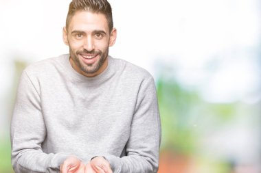 Genç yakışıklı adam giyen kazak izole üzerinden alma veya jest vererek birlikte el avuç içi ile gülen arka plan. Ayrı tutma ve koruma