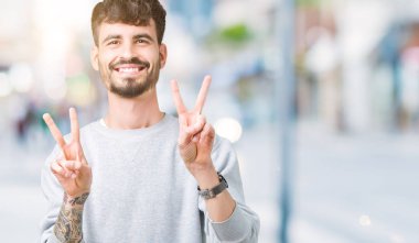 Zafer işareti yapıyor parmak gösterilen kamera seyir gülümseyen izole arka plan üzerinde sweatshirt giyen genç yakışıklı adam. İki numaralı.