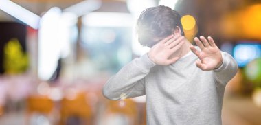 Üzerinde sweatshirt giyen genç yakışıklı sportif adam izole elleriyle gözlerini kapsayan arka plan ve stop jest ile acı ve korku ifadesi. Utandım ve negatif kavramı.
