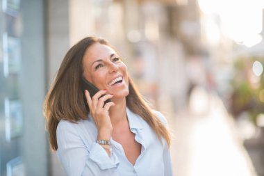 Güzel orta yaş İspanyol kadın ayakta yüzünde gülümseme ile sokağın Evet. Güneşli bir günde kendine güvenen ve neşeli gülen üzerinden yürüyüş.