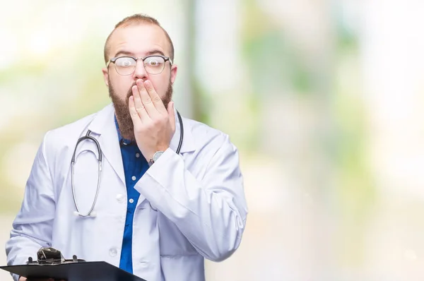 Young doctor man holding clipboard over isolated background cover mouth with hand shocked with shame for mistake, expression of fear, scared in silence, secret concept
