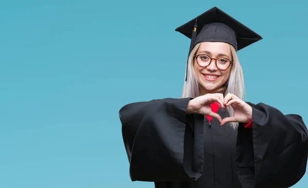 年轻的金发女子穿毕业制服在孤独的背景微笑在爱显示心脏符号和形状与手 浪漫概念 — 图库照片